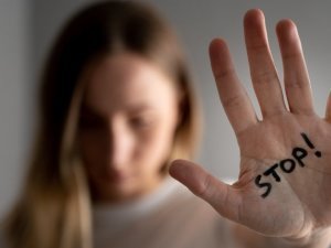Woman with bruises on her face showing stop sign, palm in focus.